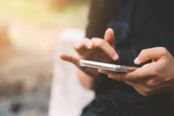 Cierre hasta la mujer de la mano utilizando el teléfono inteligente en el fondo de la calle parque al aire libre . — Foto de Stock