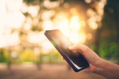 Kadın eli açık doğa Park günbatımı gökyüzü arka plan ile akıllı telefon kullanma.