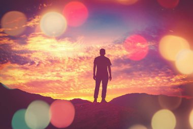 Dağın tepesinde duran bir adam gün batımı gökyüzü ve renkli Bokeh ışığı soyut arka planıyla. Özgürlük iyi hissettiriyor ve seyahat macerası tatili konsepti. 