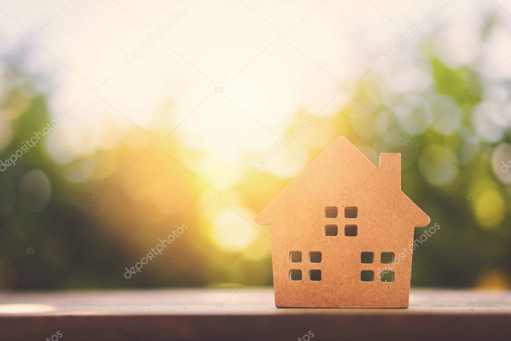 Small home model on wooden table with nature green bokeh abstract background. Family life and business real estate concept.