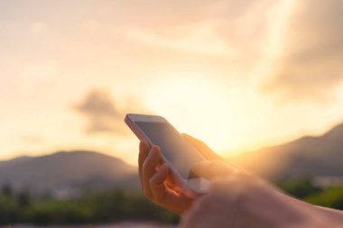 Kadın el günbatımı gökyüzü arka plan ile dağın zirvesinde akıllı telefon kullanma.