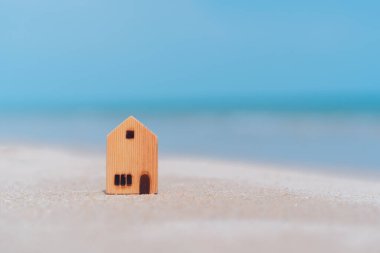 Kum sahilinde mavi gökyüzü ve beyaz bulutlarla kaplı küçük bir ev modeli. Aile yaşam tarzı ve iş yeri konseptinin kopyası. Klasik ton filtre efekti renk biçimi.