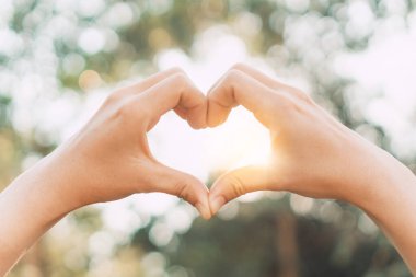 Doğada kadın eli kalp şekli Bokeh güneş ışığı parıltısı ve bulanık yaprak soyut arka plan. Mutlu aşk ve özgürlük kavramını kopyala. Klasik ton filtresi renk biçimi.