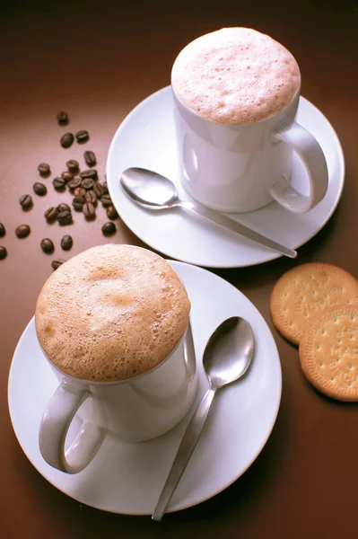 Coffee with foam cover on top surrounded with coffee beans and biscuit