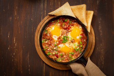 Haşlanmış domatesli sahanda yumurta, dökme demir tava, ahşap bir masa, üst manzara, kırsal, yatay