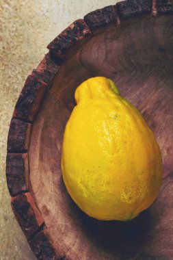 Canlı sarı bir limon, ahşap bir kasede tek başına oturuyor ve doğal yapısını sessiz bir arka plana vuruyor. Tazelik ve basitliği çağrıştırıyor..