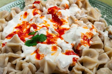 Tabakta, üzerinde kadife yoğurt ve yeşil aksanlı güzel hazırlanmış bir tabakta sergilenen baharatlı kırmızı sos bulunan bol miktarda Türk hamur köftesi yer alıyor..