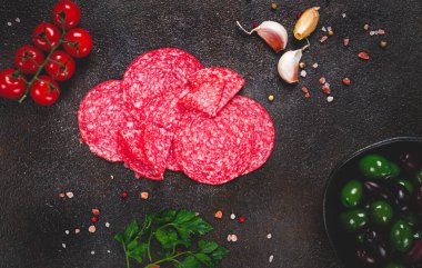 Dilimlenmiş salam, taze domates, sarımsak ve yeşil zeytin karışımı, koyu bir yüzeyde, aperatif, insan yok.,