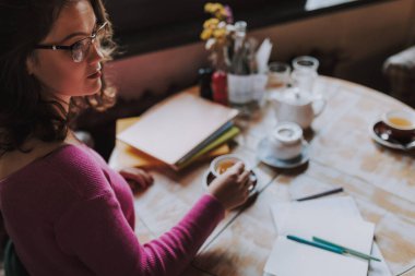 Çekici bir kadın kafeteryada tek başına oturmuş çay kaşığıyla çay karıştırıyor.