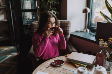 Güzel bayan pencereden bakıyor ve işten sonra kafede dinlenirken elinde çayla bardağı tutuyor.