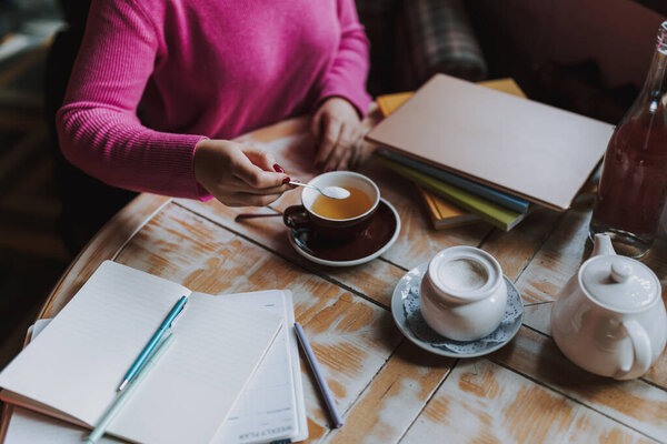 Обрезанная фотография дамы, сидящей в кафе, кладущей сахар в чай в кафе и отдыхающей
