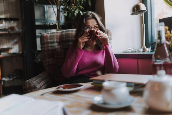 Kafedeki masada oturup çay içen ve pencereden dışarı bakan güzel genç bir kadın.