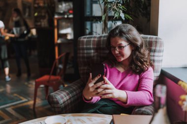 Akıllı telefon tutan ve kahve evinde dinlenirken selfie çeken mutlu genç bayan.