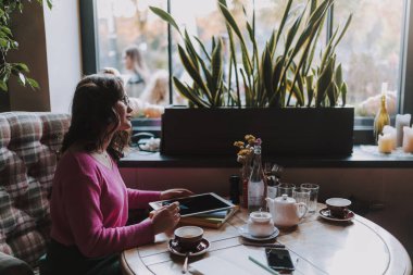Kahve dükkanında masada otururken dijital tabletle çalışan güzel bayanın yan görüntüsü
