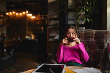Pencerenin yanındaki kafede ders çalışırken dinlenen ve kahve içen güzel bir bayan.