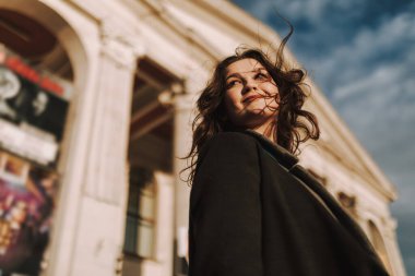 Arka planda bina ile cadde boyunca yürüyen mutlu güzel bayanın alçak açılı görüntüsü.