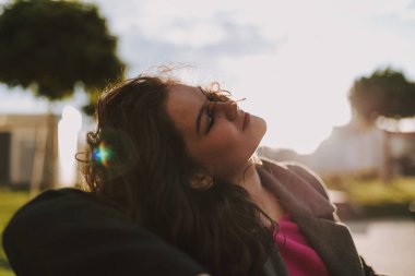 Parkta oturup güneşin altında dinlenen mutlu, gözleri kapalı güzel bir bayan.