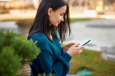 Dışarıdaki akıllı telefon ekranına bakan sevimli genç bir öğrencinin yan görünümü.