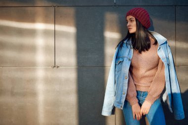 Omuzlarının üzerinde kot ceketli çekici, ince bir bayan ve bir caddede duran kafasında bere örüyor.