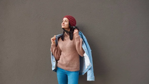 Hoş, şık giyinmiş genç bir bayan, büyük bir duvarın yanında kendini kot cekete sarıp sarmalıyor.