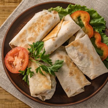 Peynirli, sebzeli ve kırsal bir tabakta yeşillikli sıcak pita ekmeği. Domates, biber, marul ve maydanozla servis edilir. Öğle yemeği için mükemmel, iş yemeği için mi yoksa yemek için mi?.