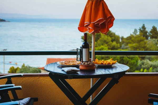 Table with a parasol on the terrace overlooking the sea, lake, ocean. Table served with fruits, olives and fried cheese. A place to relax with great views.
