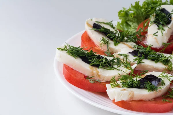 Caprese salatası düşük kalorili soğuk İtalyan aperatifi. Tabakta üç malzeme var: domates, mozzarella ve fesleğen..