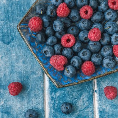 Yemek arkaplanı. Mavi arka planda yabanmersinli etno tabak, ahududu..