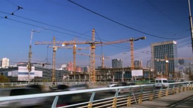 Yoğun vinçlerle dolu büyük bir inşaat alanının zaman çizelgesi, bir alışveriş merkezi inşaatında çalışan işçiler, yoğun bir yol ve ön planda yayalar..