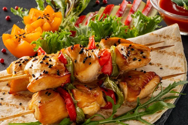 Lokantada yemek servisi yap. Yemek posteri, büyük porsiyon susamlı tavuk kebabı ve ketçap. Marul, kırmızı dolma biber, salatalık ve domates. Siyah bir taş servis tahtasına servis edilmiş..