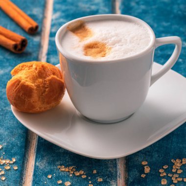 Bir fincan kapuçino, ekinoz, çilek ve tarçınlı çubuklar mavi ahşap bir arka planda.