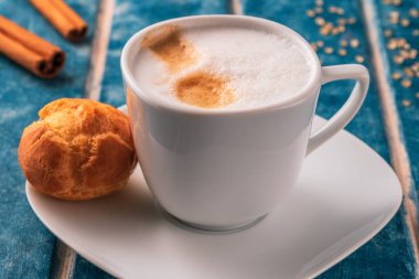 Bir fincan kapuçino, ekinoz, çilek ve tarçınlı çubuklar mavi ahşap bir arka planda.