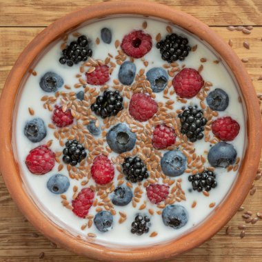 Yaban mersinli yoğurt, ahududu, böğürtlen, kil kasede keten tohumu. Vejetaryen yemeği. Sağlıklı kahvaltı, sağlıklı yemek. Restoranların, kafelerin menüsü için arka plan.