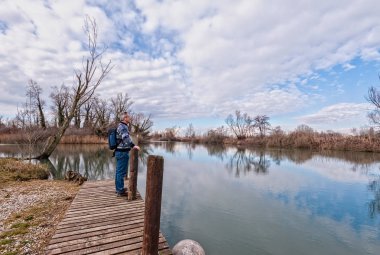 Doğa manzarası. Nehir kıyısındaki tahta iskelenin üzerinde sırt çantalı yaşlı bir yürüyüşçü..