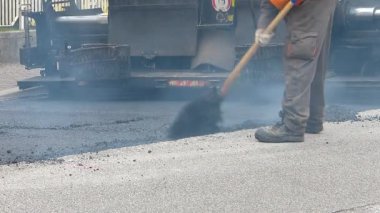 İnşaat altında kentsel yol, devam eden asfaltlama. Mavi ve turuncu üniformalı bir kürek ile işçi