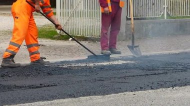İnşaat altında kentsel yol, devam eden asfaltlama. Mavi ve turuncu üniformalı bir kürek ile işçi