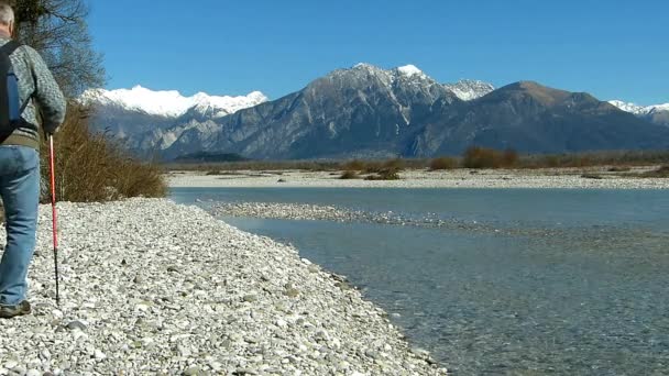 徒步旅行者走在河边 男子约60岁 在背景景观的阿尔卑斯山山 — 图库视频影像