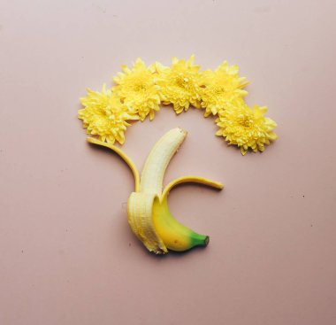 Yarım soyulmuş sarı muz, pembe arka planda izole edilmiş, üzerinde sarı çiçekler var. Kapatın. Düz yatıyordu.