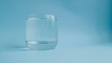 Mavi zemin üzerinde temiz temiz su bulunan küçük bir cam deney şişesi. Su içme ihtiyacı. Düzgün beslenme. Sabah alışkanlığı.