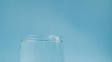  Açık mavi zemin üzerinde temiz temiz su bulunan küçük bir cam deney şişesinin tepesinde. Su içme ihtiyacı. Düzgün beslenme. Sabah alışkanlığı.