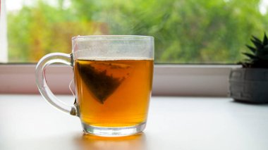 Pencere pervazında sıcak çay olan cam bardak. Çay poşetleri. Piramit çayı. Bardaktan buhar çıkıyor. Lezzetli kokulu çay partisi. Aile eğlencesi.