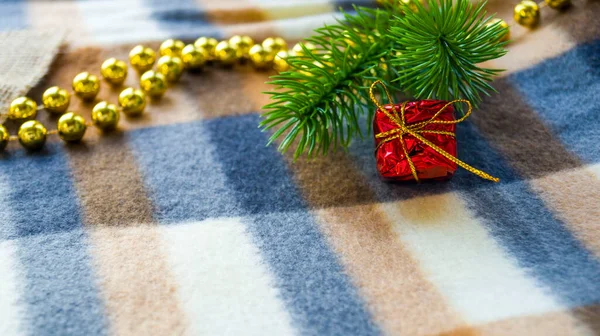 Nuovo anno e biglietto di Natale. Decorazioni natalizie su una coperta. Un piccolo regalo rosso in rami di abete rosso e perline si trovano su una coperta invernale. Posto per il testo. Ricevuto. Focus selettivo. — Foto Stock