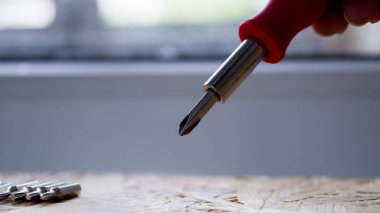 Bir çift küçük tornavida. Arka planda küçük bir tornavidanın başlığı. Cihazları tamir etmek için bir takım aletler. Tornavida kontrplağın üzerinde duruyor..