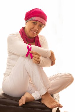 Beyaz arka planda göğüs kanserinin sembolü olarak, İspanyol bir kadın pembe kurdeleyi eliyle kaldırıyor.