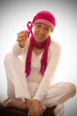 Beyaz arka planda göğüs kanserinin sembolü olarak, İspanyol bir kadın pembe kurdeleyi eliyle kaldırıyor.