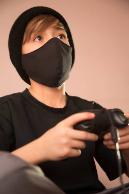 Çocuk video oyunları oynuyor, koruyucu maske kullanıyor.