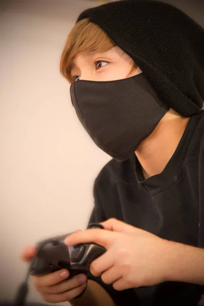 Çocuk video oyunları oynuyor, koruyucu maske kullanıyor.
