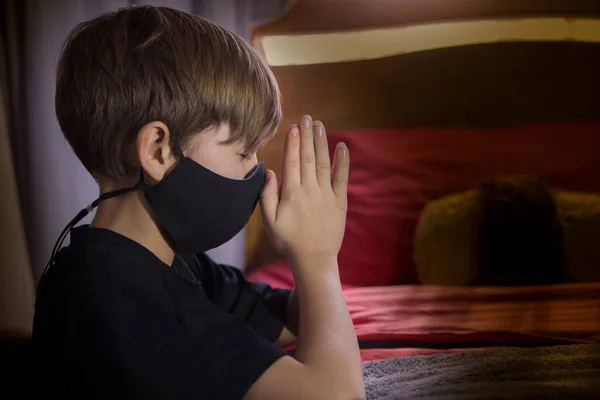 child praying at night, asking for the healing of the world, he uses cover mask due pandemic