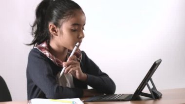 Esmer kız iPad cihazıyla ödev ve dersler veriyor ve kameraya gülümsüyor.
