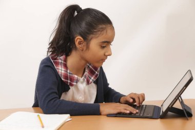 Esmer kız iPad cihazıyla ödev ve dersler veriyor ve kameraya gülümsüyor.